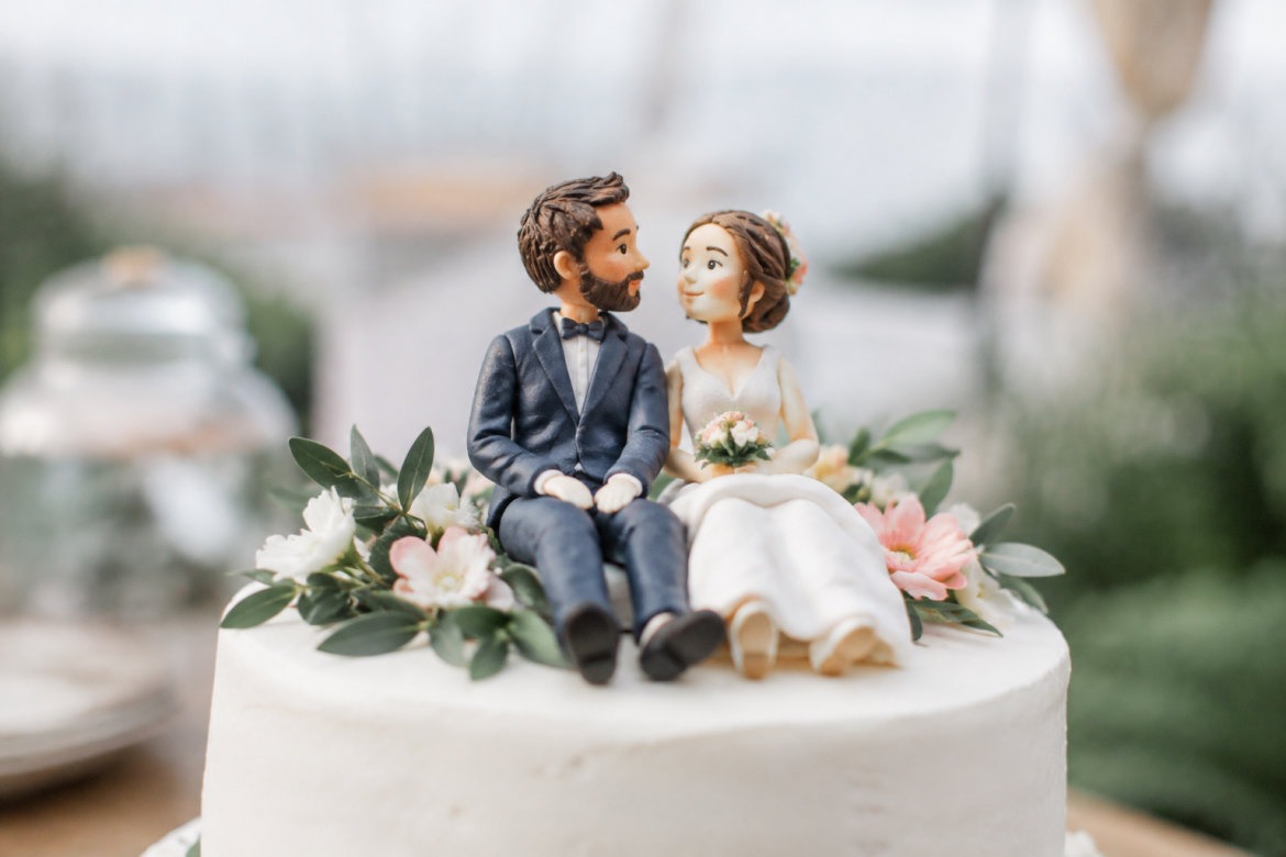 Figurines mariés personnalisées posées au sommet d'un gâteau de mariage blanc à étages
